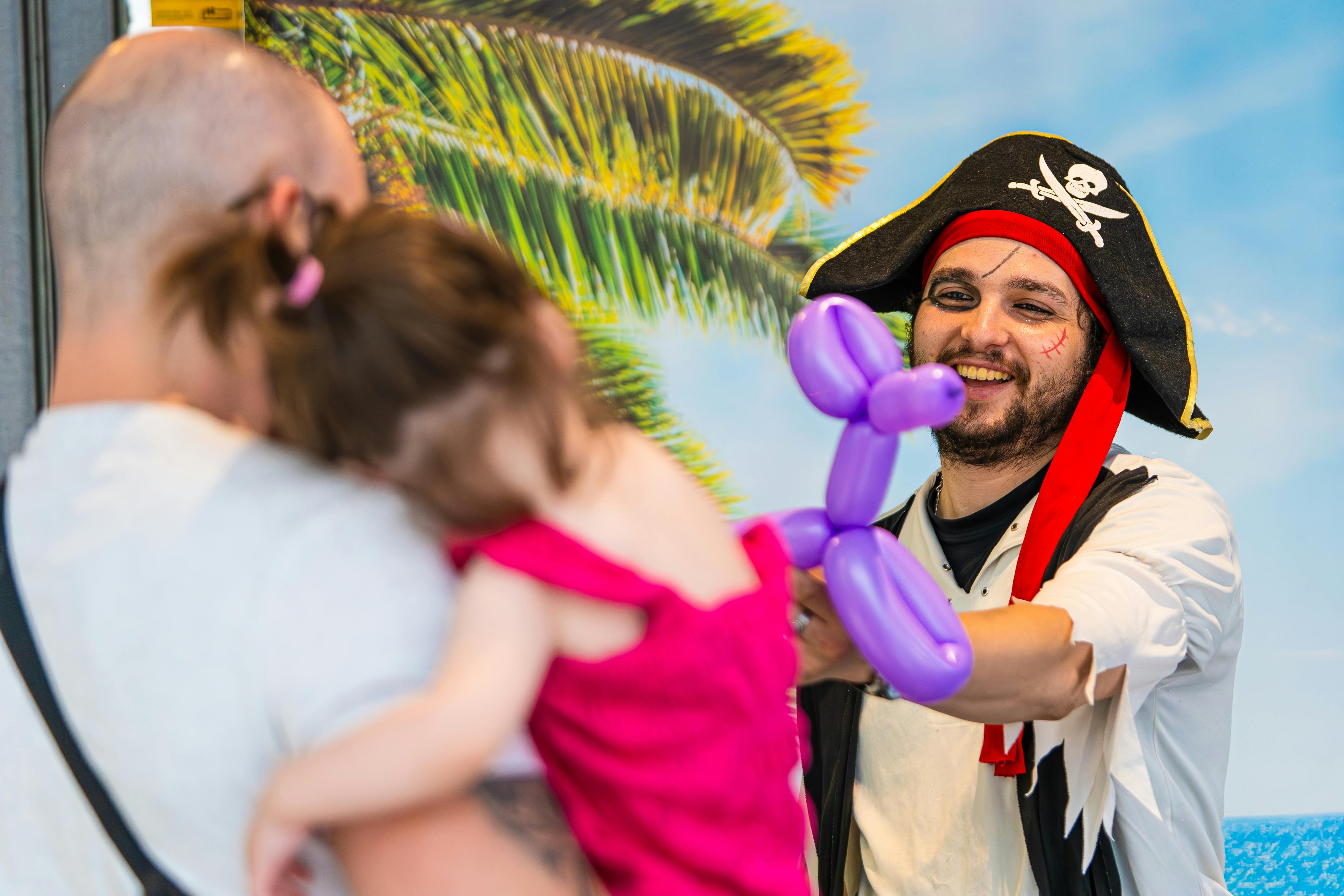 pexels-photo-26763705-26763705 Pirate entertainer gifting a balloon animal to a little girl during a fun outing.
